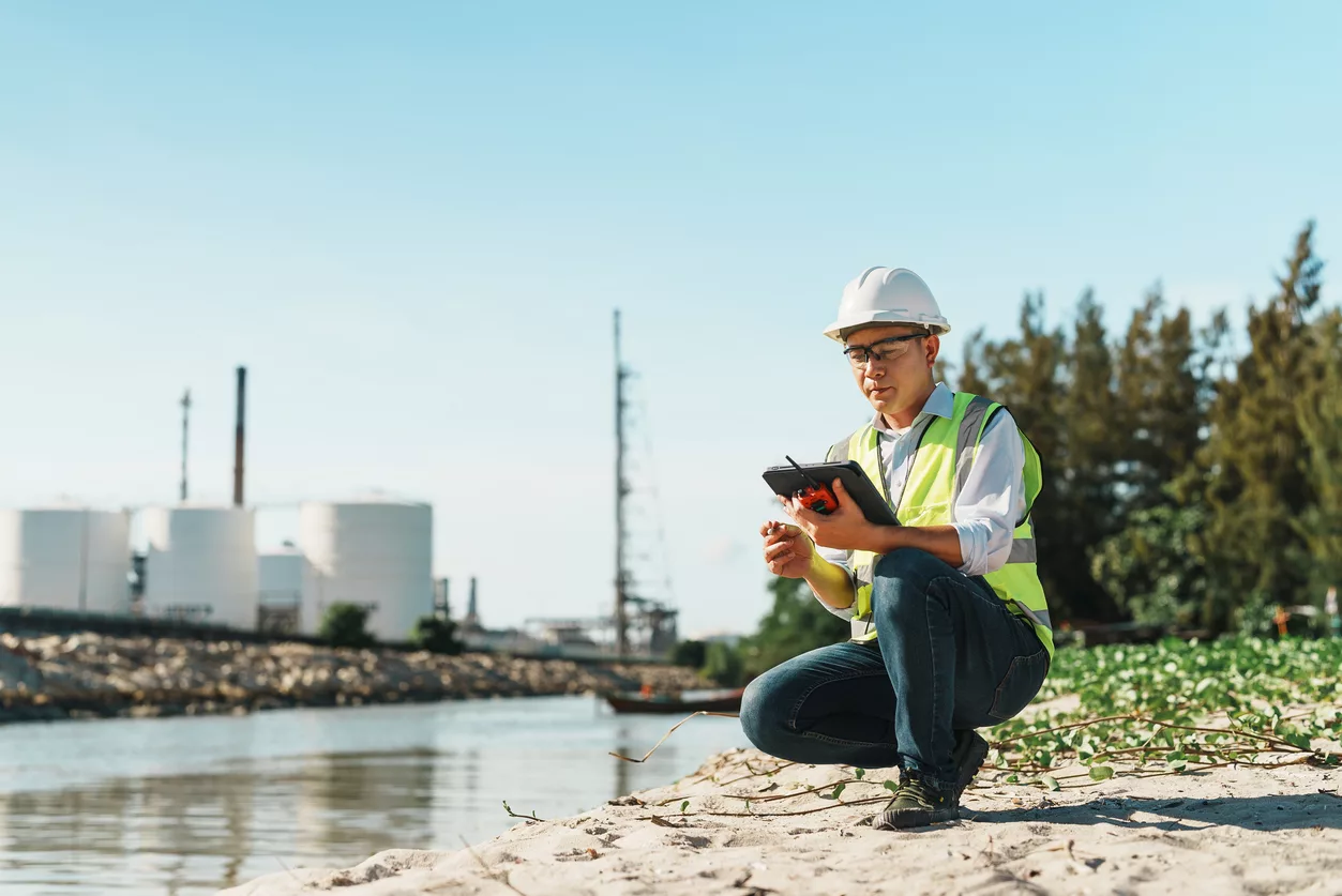 Male petroleum refinery engineer uses tablet to check work at a beachside job site.