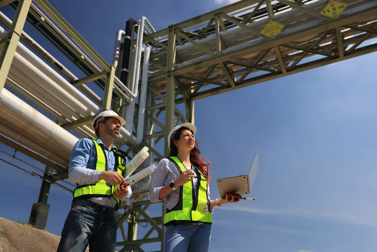 Female and male piping system engineers working at the pipeline construction in the refinery or chemical plant at an industrial estate